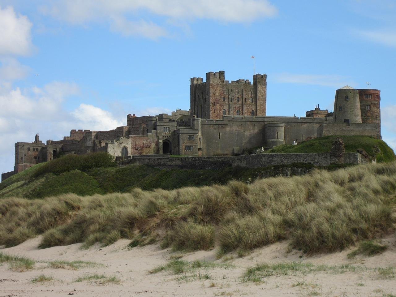 Medieval castle on a hilltop surrounded by grassy sand dunes under a partly cloudy sky.